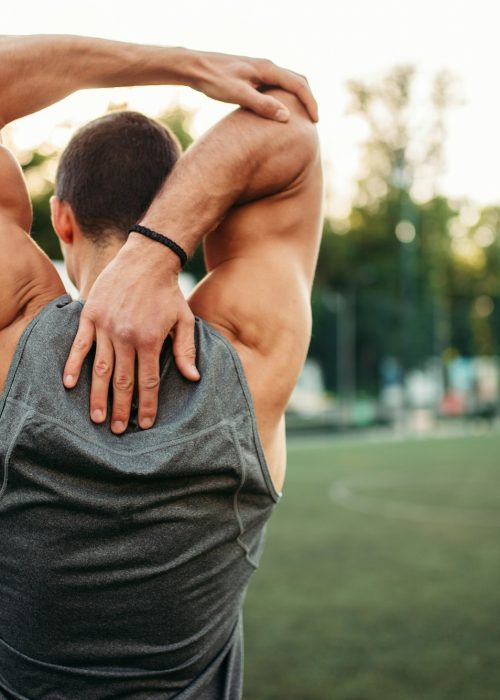 Male athlete doing stretching exercise, back view